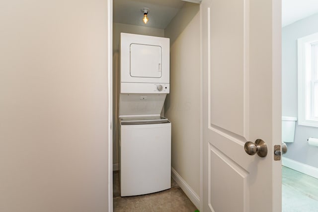 clothes washing area featuring laundry area, baseboards, and stacked washer / dryer