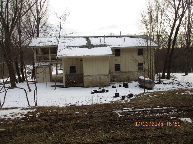 snow covered property with stone siding, a shed, and board and batten siding