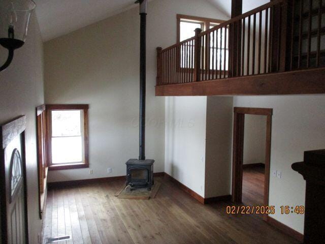 unfurnished living room featuring baseboards, visible vents, wood finished floors, a wood stove, and high vaulted ceiling