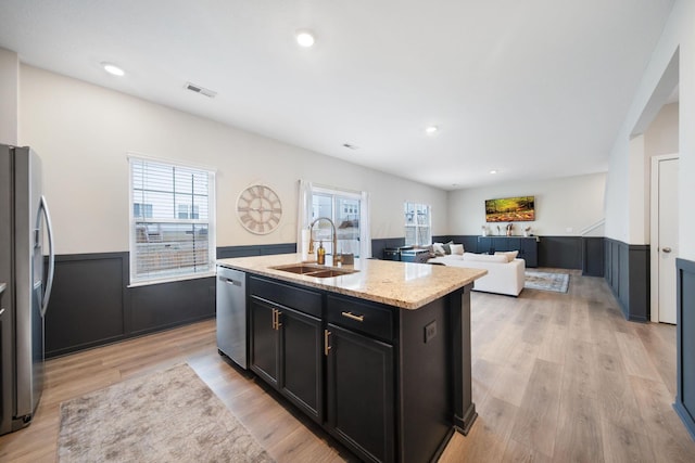 kitchen featuring wainscoting, light wood-style flooring, light stone counters, stainless steel appliances, and a sink