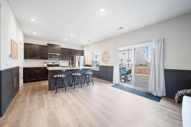 kitchen featuring a breakfast bar area, visible vents, appliances with stainless steel finishes, light wood-style floors, and dark brown cabinetry