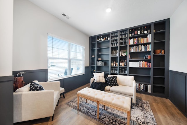 sitting room with a wainscoted wall, visible vents, and wood finished floors