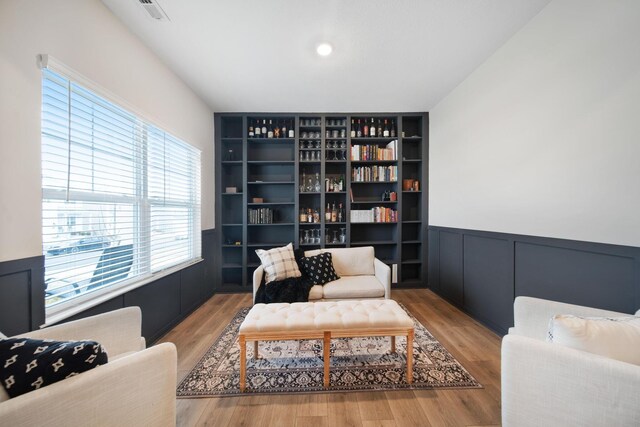 living area featuring visible vents, wainscoting, wood finished floors, built in shelves, and a decorative wall