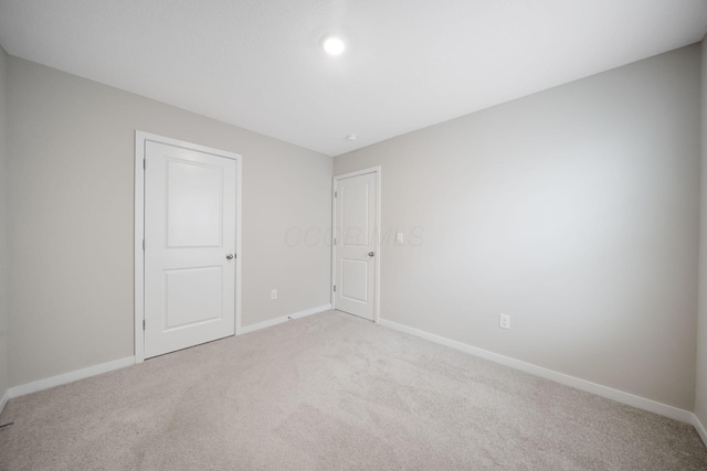 spare room with baseboards and light colored carpet