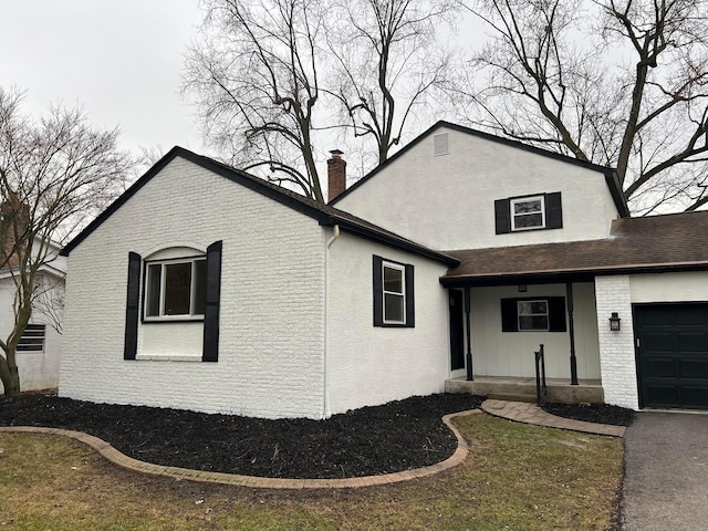 view of side of property featuring roof with shingles, brick siding, a chimney, and an attached garage