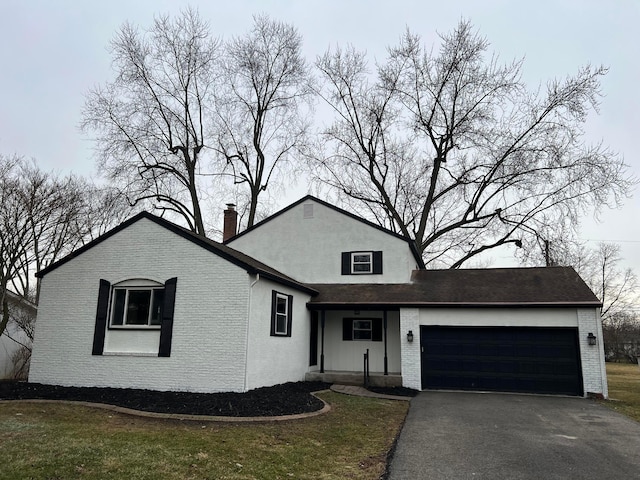 view of front of property featuring an attached garage, brick siding, driveway, a chimney, and a front yard