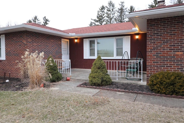 property entrance with a shingled roof, covered porch, and brick siding