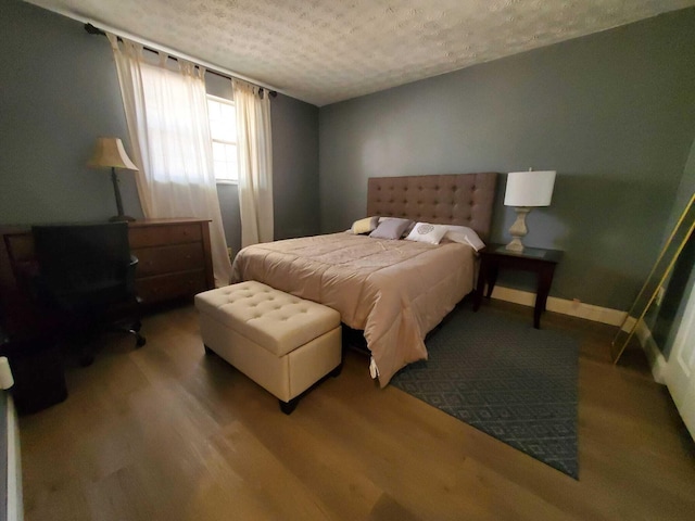 bedroom with wood finished floors, baseboards, and a textured ceiling