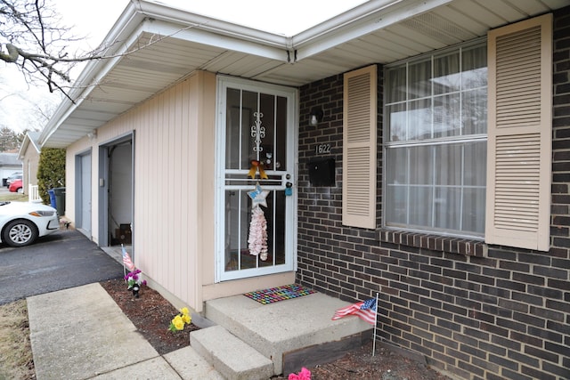 property entrance with brick siding, an attached garage, and driveway