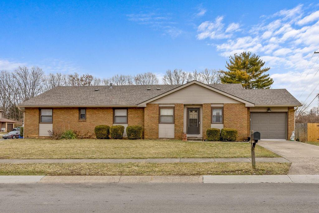 ranch-style home with a garage, a shingled roof, concrete driveway, a front lawn, and brick siding