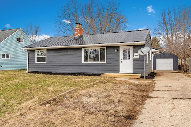 view of front of property featuring a garage, concrete driveway, a chimney, metal roof, and an outbuilding