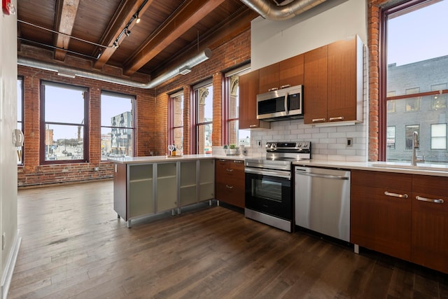 kitchen with dark wood-style flooring, stainless steel appliances, a sink, brick wall, and a peninsula