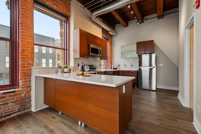 kitchen featuring appliances with stainless steel finishes, dark wood-style flooring, a peninsula, and tasteful backsplash