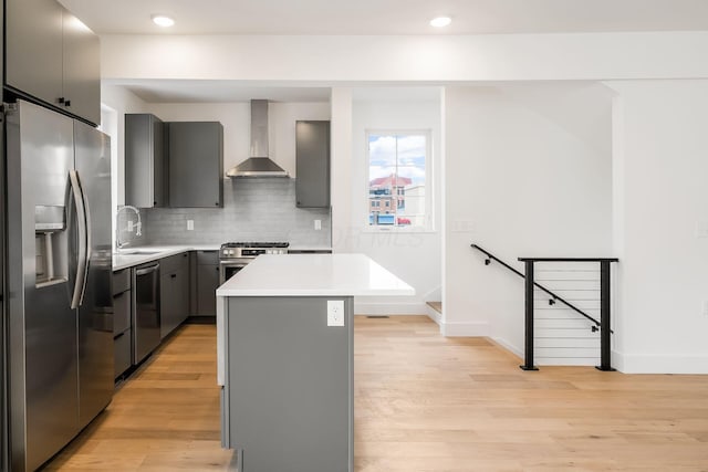 kitchen with light wood-style flooring, stainless steel appliances, gray cabinetry, wall chimney range hood, and a sink