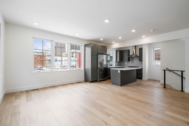 kitchen with light wood finished floors, light countertops, wall chimney range hood, and stainless steel fridge with ice dispenser