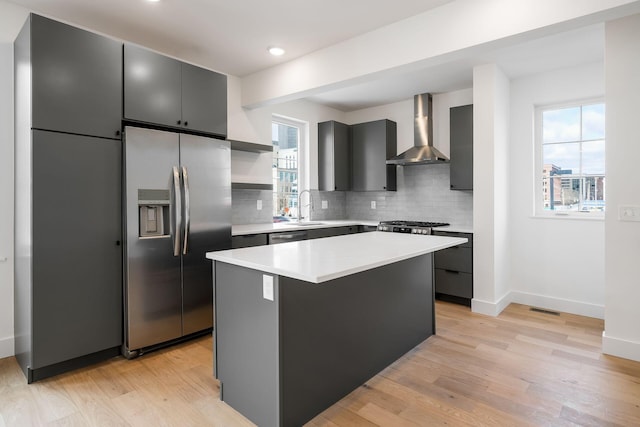 kitchen featuring a sink, light countertops, wall chimney range hood, appliances with stainless steel finishes, and light wood-type flooring