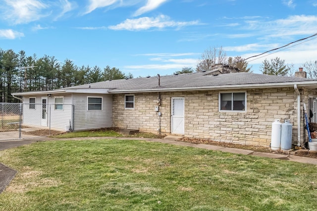 back of house featuring roof with shingles, a yard, a chimney, fence, and stone siding