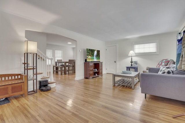 living room with baseboards, arched walkways, visible vents, light wood-style flooring, and stairs