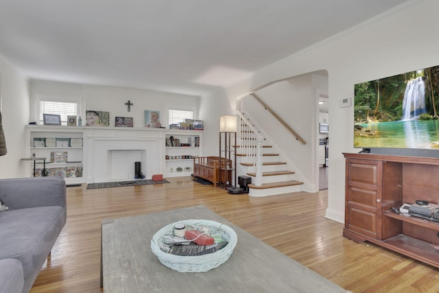 living area with a healthy amount of sunlight, a brick fireplace, stairs, and wood finished floors