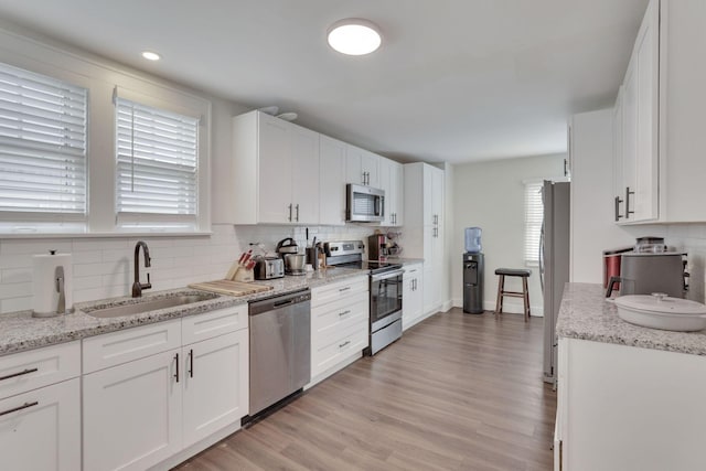 kitchen with appliances with stainless steel finishes, a sink, light stone countertops, and white cabinets