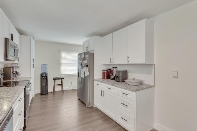 kitchen featuring stainless steel appliances, light wood finished floors, white cabinetry, and light stone countertops