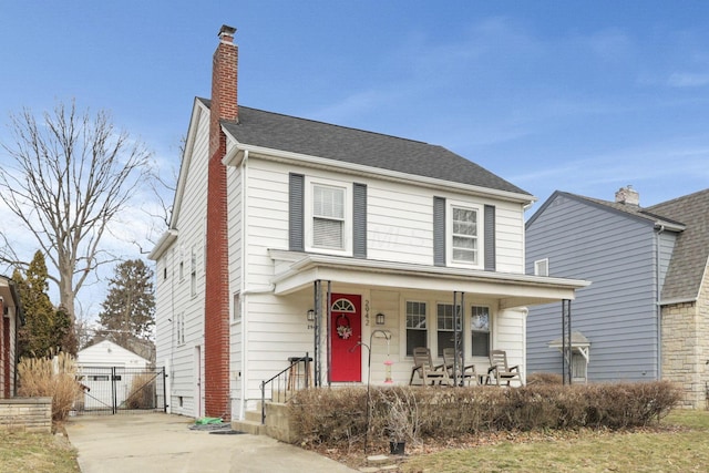 view of front of house featuring covered porch, a shingled roof, concrete driveway, a gate, and a chimney