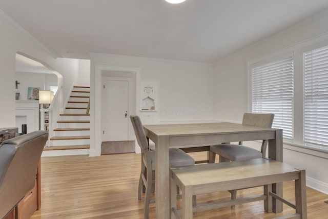 dining room with baseboards, arched walkways, stairs, crown molding, and light wood-type flooring