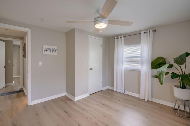 spare room featuring ceiling fan, light wood finished floors, and baseboards