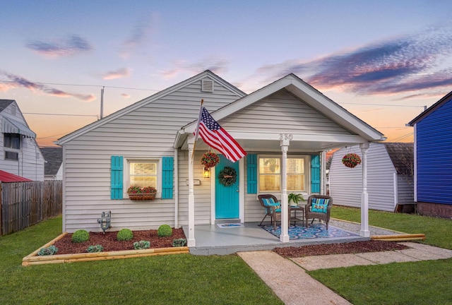 bungalow-style home featuring covered porch, a yard, and fence