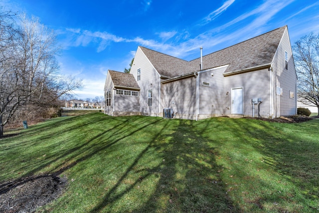 rear view of property with roof with shingles, a lawn, and central AC