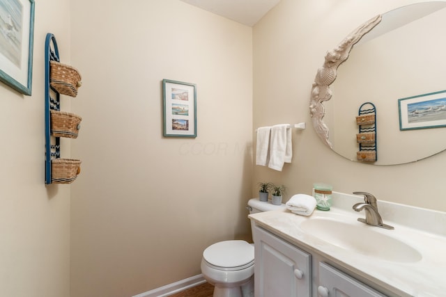 half bathroom with baseboards, vanity, and toilet