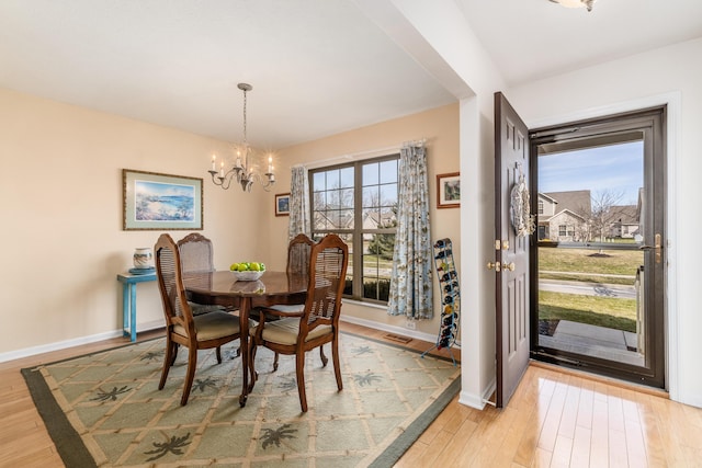 dining room with light wood finished floors, an inviting chandelier, visible vents, and baseboards