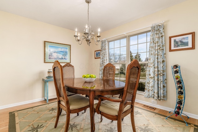 dining room with baseboards, light wood finished floors, visible vents, and an inviting chandelier