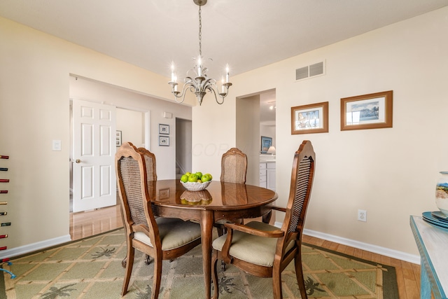 dining space featuring visible vents, a notable chandelier, baseboards, and wood finished floors