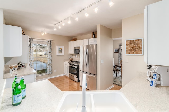 kitchen featuring light countertops, appliances with stainless steel finishes, light wood-style floors, white cabinets, and a sink