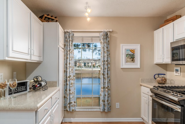 kitchen featuring baseboards, white cabinetry, appliances with stainless steel finishes, and a textured ceiling