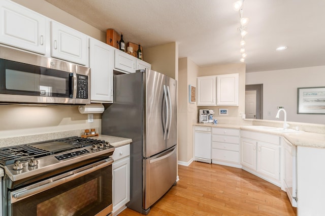 kitchen with light wood-style flooring, appliances with stainless steel finishes, light countertops, white cabinetry, and a sink