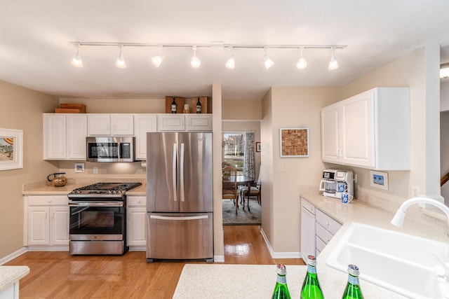 kitchen featuring stainless steel appliances, light countertops, light wood-type flooring, white cabinetry, and a sink