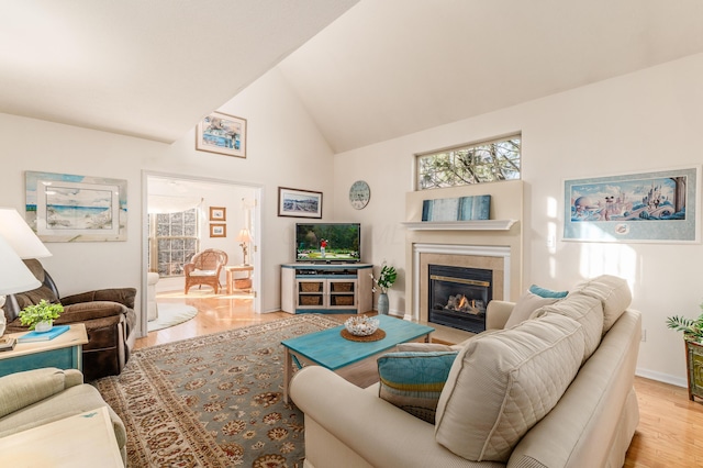 living area with baseboards, high vaulted ceiling, wood finished floors, and a glass covered fireplace