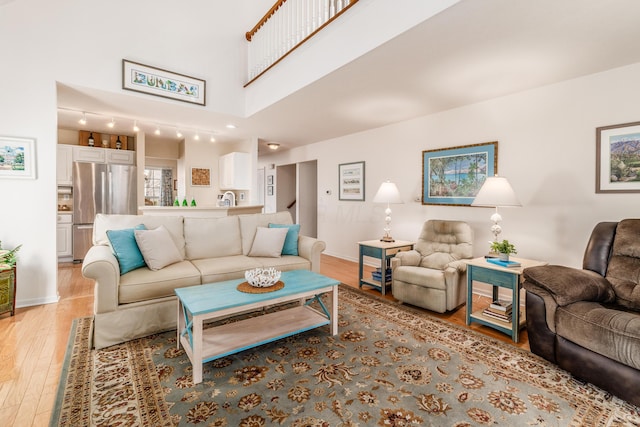 living room with a towering ceiling, light wood-style flooring, and baseboards