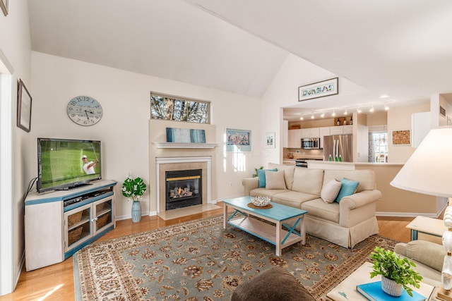 living room with light wood-type flooring, baseboards, vaulted ceiling, and a tiled fireplace