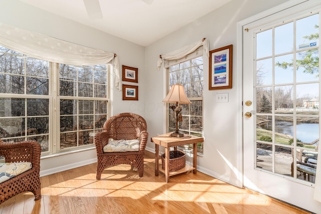 living area with baseboards, a water view, a ceiling fan, and light wood-style floors