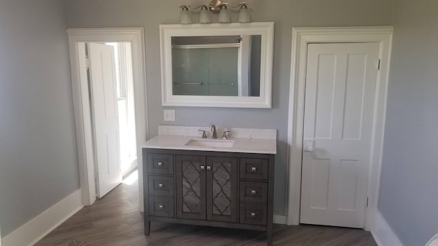 full bath with a shower with door, wood finished floors, vanity, and baseboards