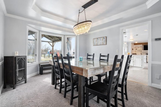 dining room featuring a notable chandelier, light colored carpet, baseboards, ornamental molding, and a raised ceiling