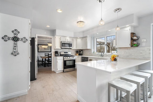 kitchen with pendant lighting, light countertops, appliances with stainless steel finishes, white cabinetry, and a peninsula