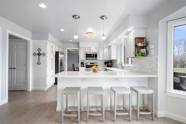 kitchen with a peninsula, appliances with stainless steel finishes, light countertops, and white cabinets