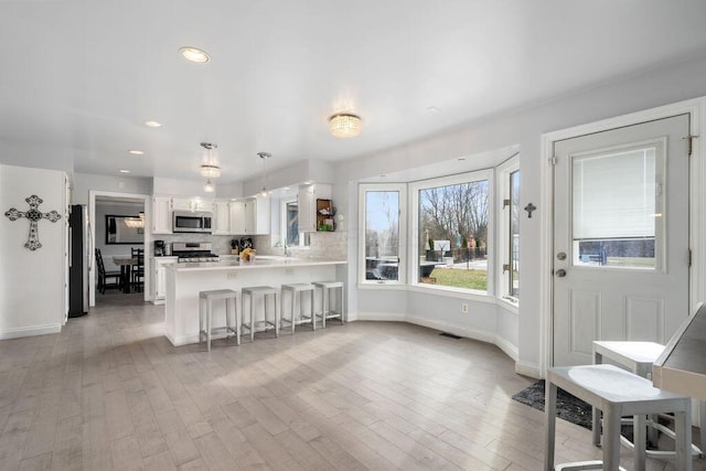 kitchen featuring pendant lighting, stainless steel appliances, light countertops, white cabinets, and a peninsula