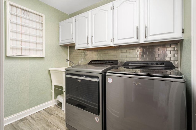 clothes washing area featuring light wood-style floors, washing machine and dryer, cabinet space, and baseboards