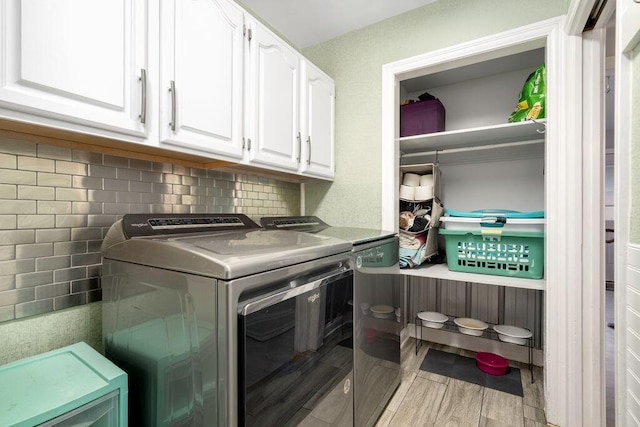 clothes washing area featuring light wood-style flooring, washer and clothes dryer, and cabinet space