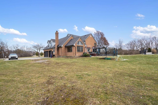 view of front of home featuring a trampoline, a chimney, an attached garage, driveway, and a front lawn